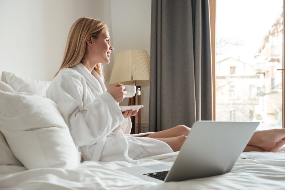 Mulher com seu notbook em cima da cama de hotel